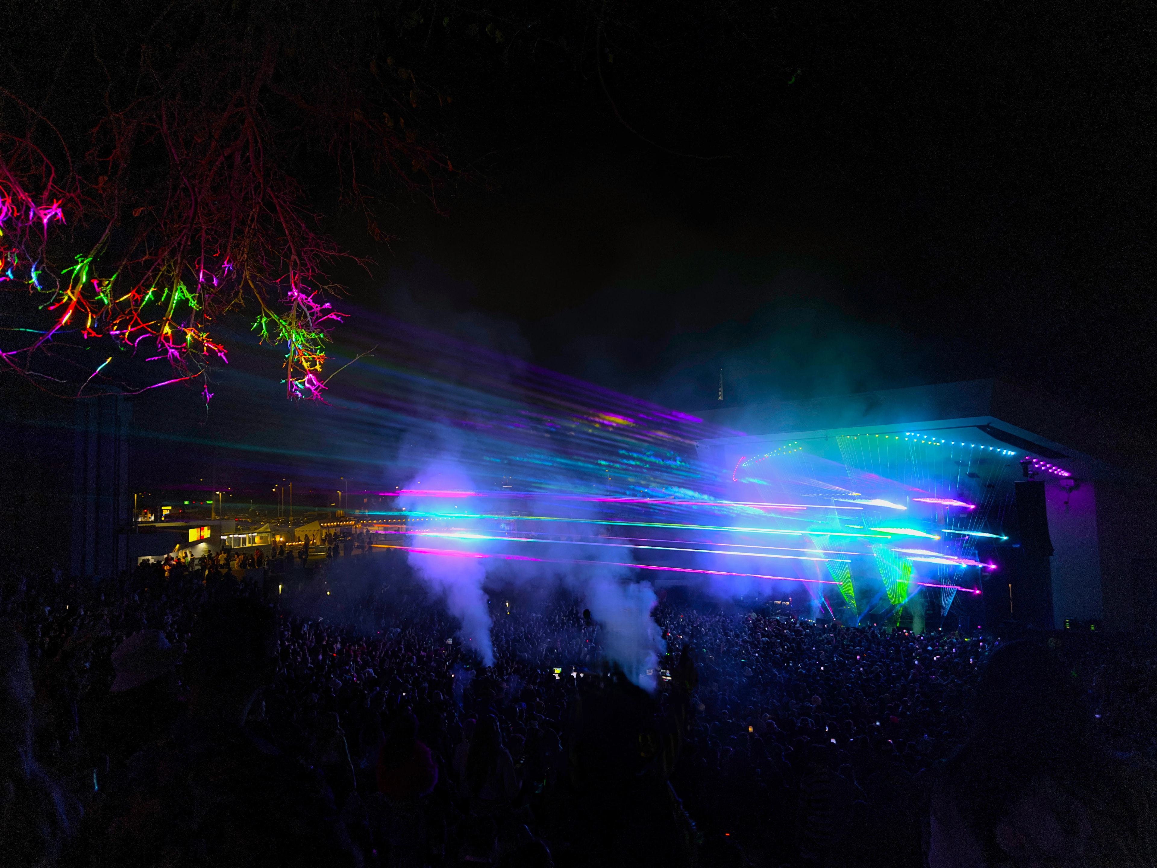 Colorful laser show fanning out over a crowd at an outdoor festival at night